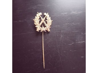 Guldpläterad insignia med gevär och lagerkrans
