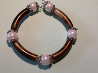 ett egenhändigt gjort armband i färgerna brun, vit och silver.