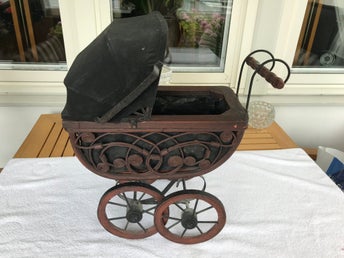 Vintage dockvagn i mörkt trä med en intrikat flätad korg och svart sufflett.
